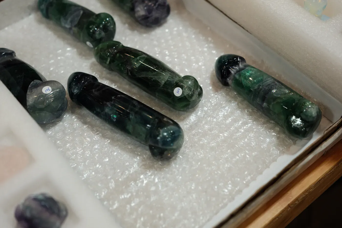Various polished stone objects are neatly displayed on white packaging material in a box.