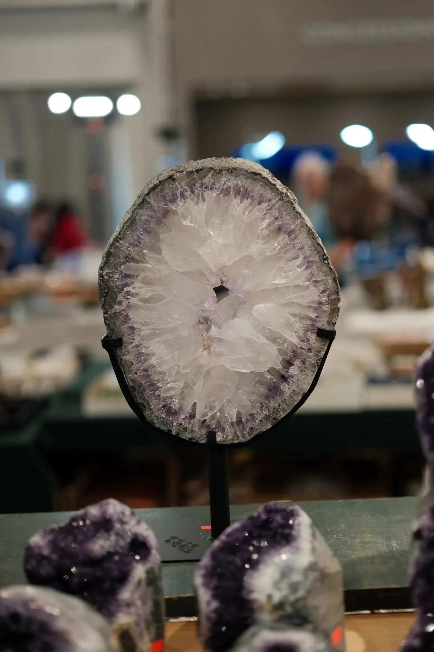 A halved geode with a crystalline interior is displayed on a stand at a market or exhibition.